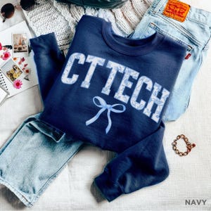 May include: Navy blue sweatshirt with a white floral pattern and the text "CTTECH" in white with a blue bow.