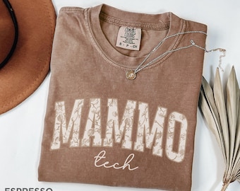 Peut inclure: Un t-shirt marron avec un motif floral qui dit "MAMMOTH tech" en lettres blanches.