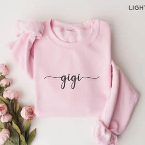 May include: Light pink sweatshirt with the word "gigi" written in black cursive script.