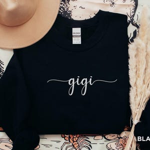 May include: Black sweatshirt with the word "gigi" written in white cursive script.