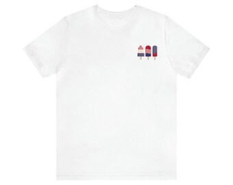 May include: White t-shirt with a graphic of three red, white, and blue popsicles.