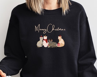 May include: Black sweatshirt with a white graphic of four cats wearing Santa hats and holding Christmas lights and a gift. The text "Meowy Christmas" is above the cats.