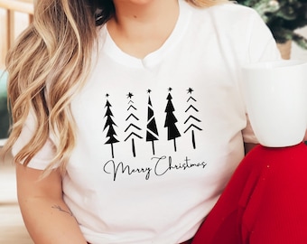 Könnte beinhalten: Weißes T-Shirt mit einer schwarzen Grafik von stilisierten Weihnachtsbäumen mit Sternen. Die Worte "Merry Christmas" sind in einer kursiven Schrift unter den Bäumen geschrieben. Das T-Shirt hat einen Rundhalsausschnitt.