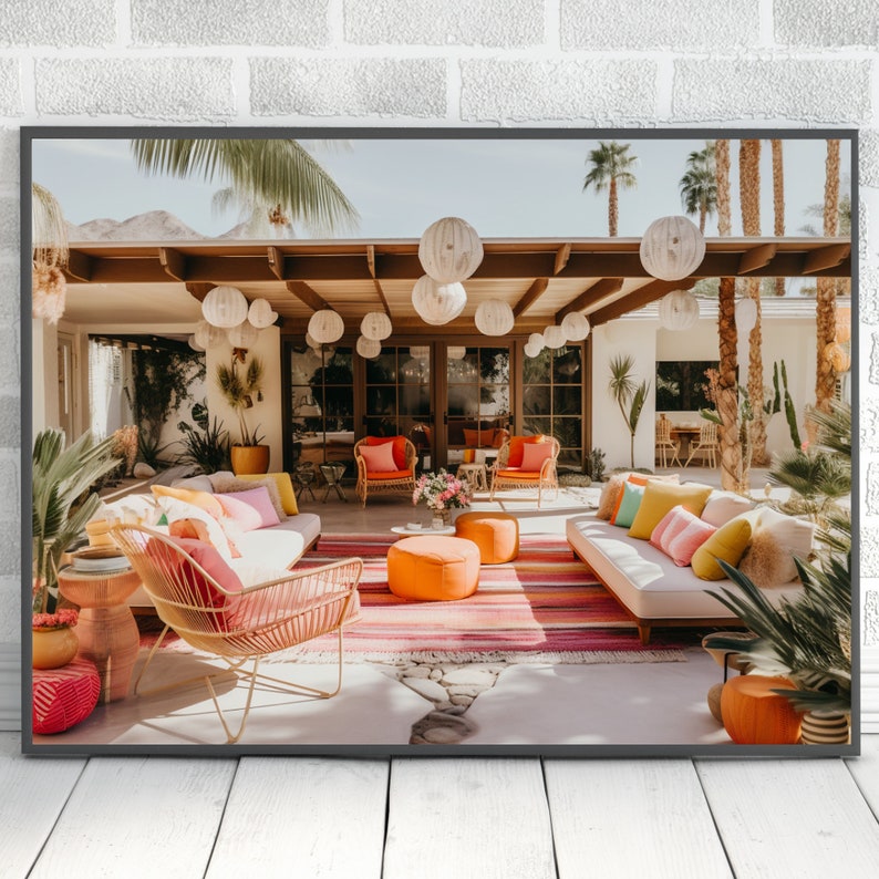 Op de afbeelding: Een patio-meubelenset met een witte bank, oranje kussens en een roze en oranje kleed. De patio is versierd met witte papieren lantaarns en weelderig groen.