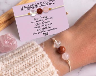 Puede incluir: Una pulsera con tres cuentas: un cuarzo transparente, una piedra de sol roja brillante y un cuarzo rosa pálido en un cordón claro. La tarjeta de presentación dice PREGNANCY y enumera las piedras con sus cualidades: amor, bondad, bienestar, energía, claridad, confianza, calma, positividad y conexión.