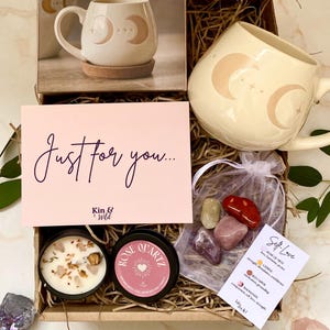 May include: A gift box containing a cream-coloured mug with a crescent moon design, a candle, a rose quartz candle, crystals, and a card reading "Just for you...". The box also includes a photo of the mug.