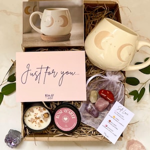 May include: A gift box containing a cream-coloured mug with a crescent moon design, a candle, a rose quartz candle, crystals, and a card reading "Just for you...". The box also includes a photo of the mug.