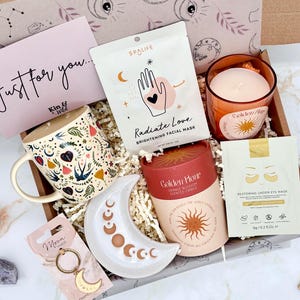 May include: A gift box containing a ceramic mug with a colourful bird and heart pattern, a SpaLife Radiate Love facial mask, a Golden Hour orange blossom candle in a glass jar, a moon-shaped trinket dish, a Golden Hour candle tube, and eye masks.