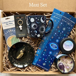 May include: A gift box labeled Maxi Set containing a dark blue celestial mug, a black ceramic dish, a rose quartz mushroom keychain, two packs of incense, a candle with crystals, a palo santo stick, and loose amethyst and rose quartz stones.