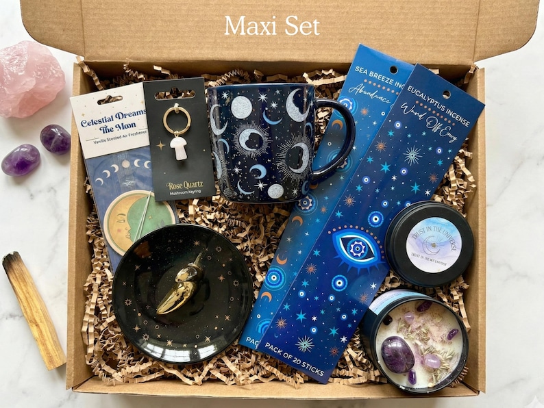 May include: A gift box labeled Maxi Set containing a dark blue celestial mug, a black ceramic dish, a rose quartz mushroom keychain, two packs of incense, a candle with crystals, a palo santo stick, and loose amethyst and rose quartz stones.