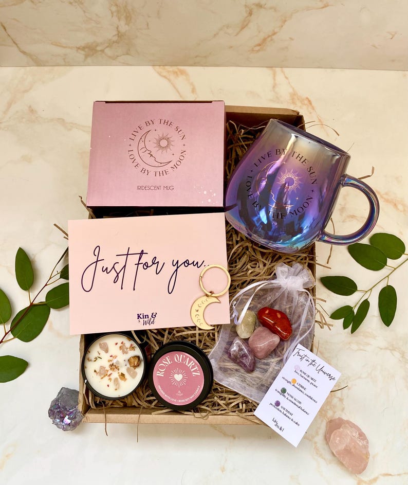 May include: A gift box with a pink box, iridescent mug, and card with text. The box also contains a candle, Rose Quartz tin, crystals, and a moon and star charm. The mug has "Live by the Sun, Love by the Moon" text.