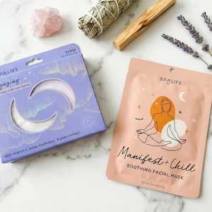 May include: A flat lay featuring spa products. A purple box of "Stargazing" eye masks and a pink "Manifest + Chill" facial mask are displayed. Additional items include a rose quartz crystal, sage bundle, palo santo stick, and lavender sprigs.