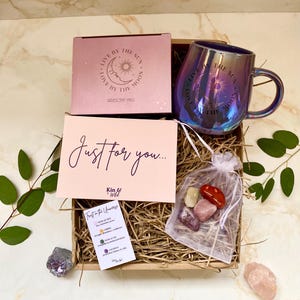 May include: A gift box with a pink iridescent mug, a pink box, a card with the text "Just for you...", a small bag of stones, and greenery. The mug has the text "Love by the moon" and "Live by the sun".