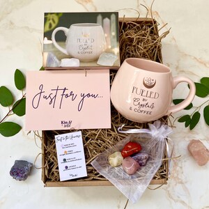 以下が含まれることがあります： 「Fueled by Crystals & Coffee」と書かれたピンク色のマグカップが入ったギフトボックス。ボックスには「Just for you...」と書かれたカードと、小さなクリスタルの袋が含まれています。マグカップの写真もあります。
