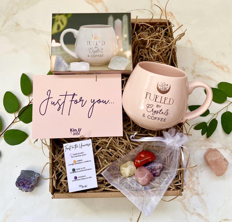 以下が含まれることがあります： 「Fueled by Crystals & Coffee」と書かれたピンク色のマグカップが入ったギフトボックス。ボックスには「Just for you...」と書かれたカードと、小さなクリスタルの袋が含まれています。マグカップの写真もあります。