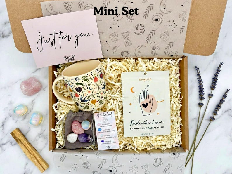 May include: A gift box labeled "Mini Set" contains a floral-decorated mug, a face mask, crystals, and a card that says "Just for you...". The box is filled with shredded paper and includes a bundle of lavender.