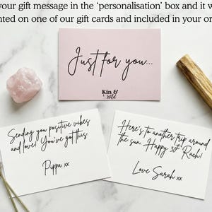 May include: Three rectangular gift cards with black cursive text, a pale pink rose quartz crystal, and a dried lavender sprig. One card reads Just for you... Kin & Wild, another says Sending you positive vibes and love! You've got this. Pippa xx, and the third reads Here's to another trip around the sun. Happy 30th Rach! Love Sarah xx.