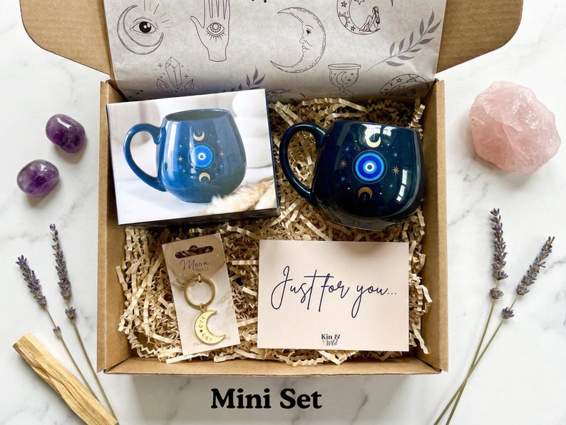 Op de afbeelding: Cadeaudoos met een donkerblauwe mok met een boze oog-ontwerp, een halve maan sleutelhanger en een kaart met de tekst "Just for you...". De doos bevat ook een rozenkwartskristal en amethiststenen. De tekst "Mini Set" staat onderaan.