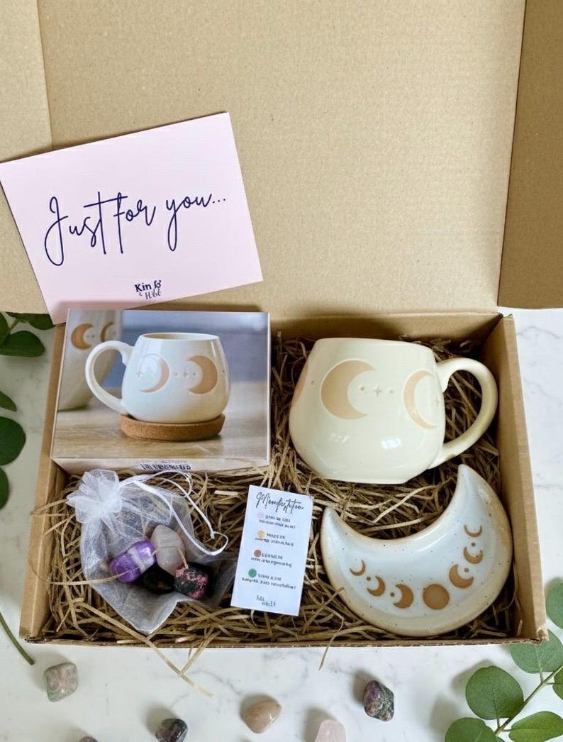 Peut inclure: Coffret cadeau contenant une tasse cr&egrave;me avec un motif de croissant de lune, un plat assorti en forme de lune, un petit sachet de cristaux et une carte avec l'inscription "Juste pour vous". Les articles sont dispos&eacute;s sur de la paille.