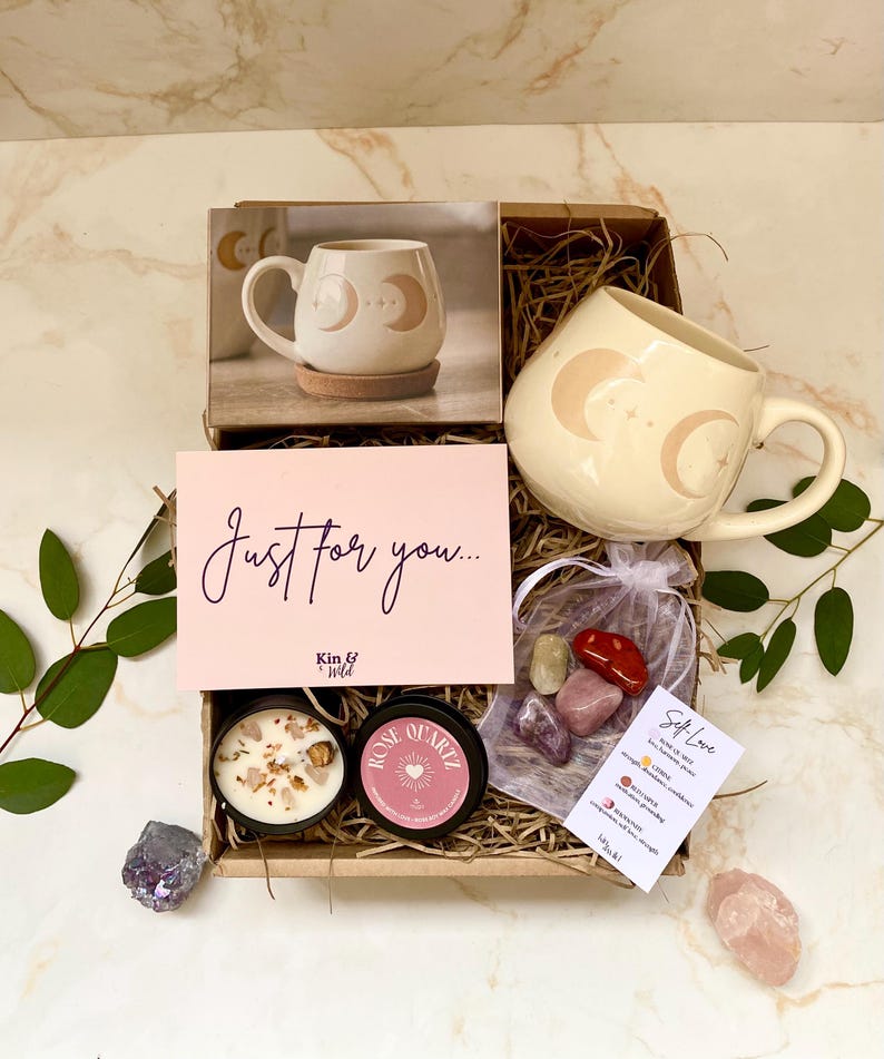 May include: A gift box containing a cream-coloured mug with a crescent moon design, a candle, a rose quartz candle, crystals, and a card reading "Just for you...". The box also includes a photo of the mug.