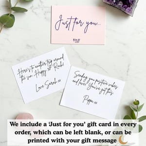 May include: Three gift cards on a marble surface. One pink card reads "Just for you..." in cursive. Two white cards have handwritten messages. Greenery and a crystal are in the background. The cards are for gifts.