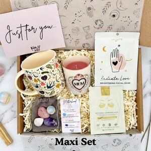 May include: A gift box with a mug, candle, facial mask, eye mask, crystals, and a card that says "Just for you." The mug and candle have floral and heart designs. The box is labeled "Maxi Set."