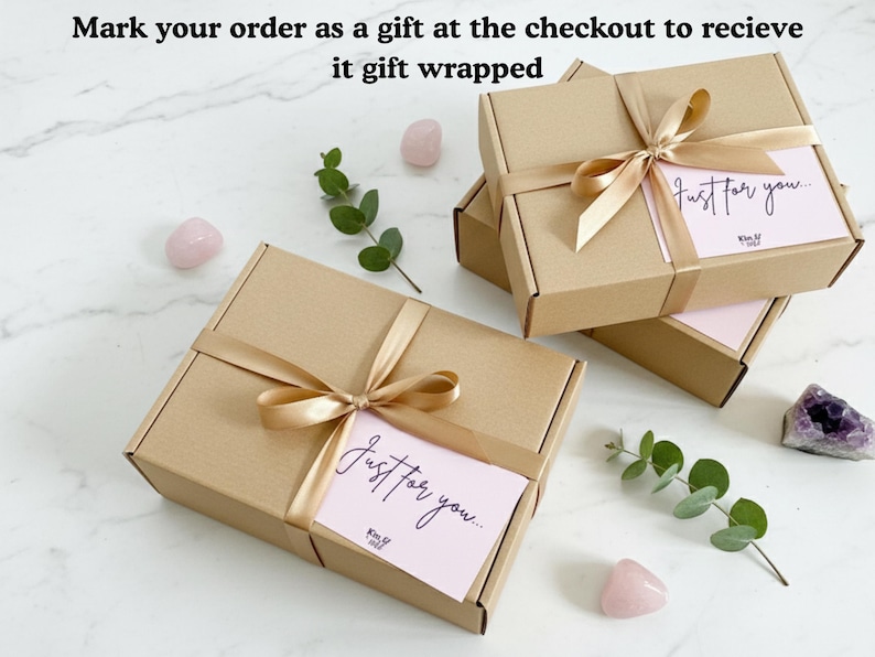 May include: Kraft gift boxes tied with gold satin ribbon and bows. Each box has a pink card with the words "Just for you..." in cursive. The boxes are arranged with pink stones and greenery on a marble surface.