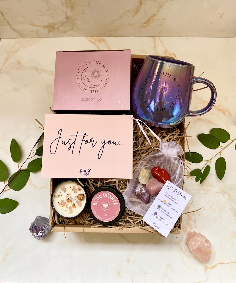 May include: A gift box containing an iridescent mug, a candle, and crystals. The mug has the text "Live by the Sun, Love by the Moon." A card reads "Just for you..." and a small bag contains crystals.