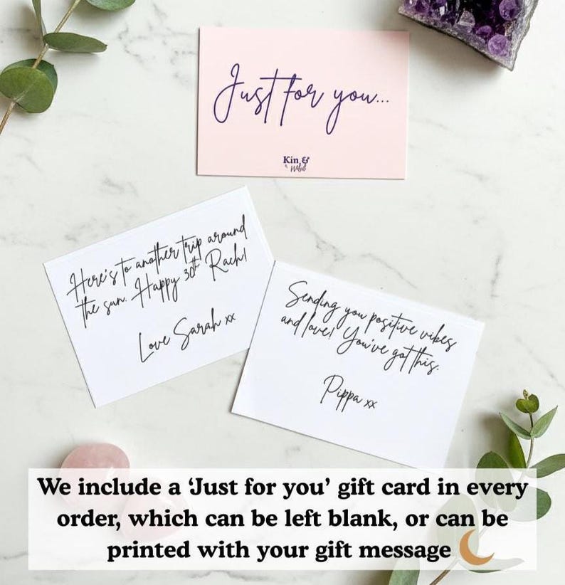 May include: A light pink gift card with the text "Just for you..." is displayed above two white cards with handwritten messages. The cards are on a marble surface, with greenery and crystals in the background.