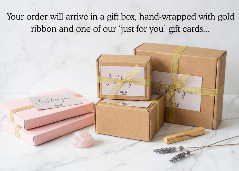 May include: Two light pink rectangular boxes and three brown cardboard boxes tied with gold ribbon. Each box features a white gift card with the text 'Just for you'. A raw rose quartz crystal, a wooden stick, and dried lavender sprigs are included.