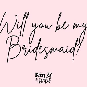 May include: A light pink background with the text "Will you be my Bridesmaid?" in elegant black script. The words "Kin & Wild" are at the bottom in a smaller, stylized font.