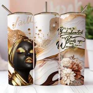 Puede incluir: Tres vasos de acero inoxidable con diseños abstractos dorados y blancos. Un vaso presenta a una mujer negra con detalles dorados y la palabra "Faith". Otro tiene el texto "He heals the brokenhearted and binds up their wounds".
