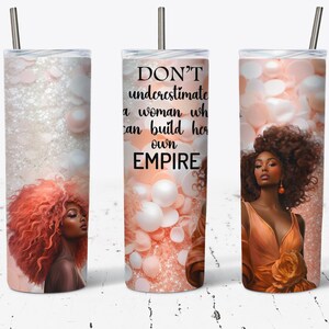 May include: A pink and white glitter tumbler with a black and white quote that reads "DON'T underestimate a woman who can build her own EMPIRE". The tumbler features a woman with brown skin and curly brown hair.