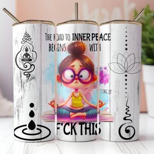 Puede incluir: Un vaso blanco con diseño de vetas de madera presenta una niña de dibujos animados en postura de yoga, con gafas. El texto dice: "El camino hacia la paz interior comienza con... F*ck this". El vaso también tiene una pajita y un borde dorado.