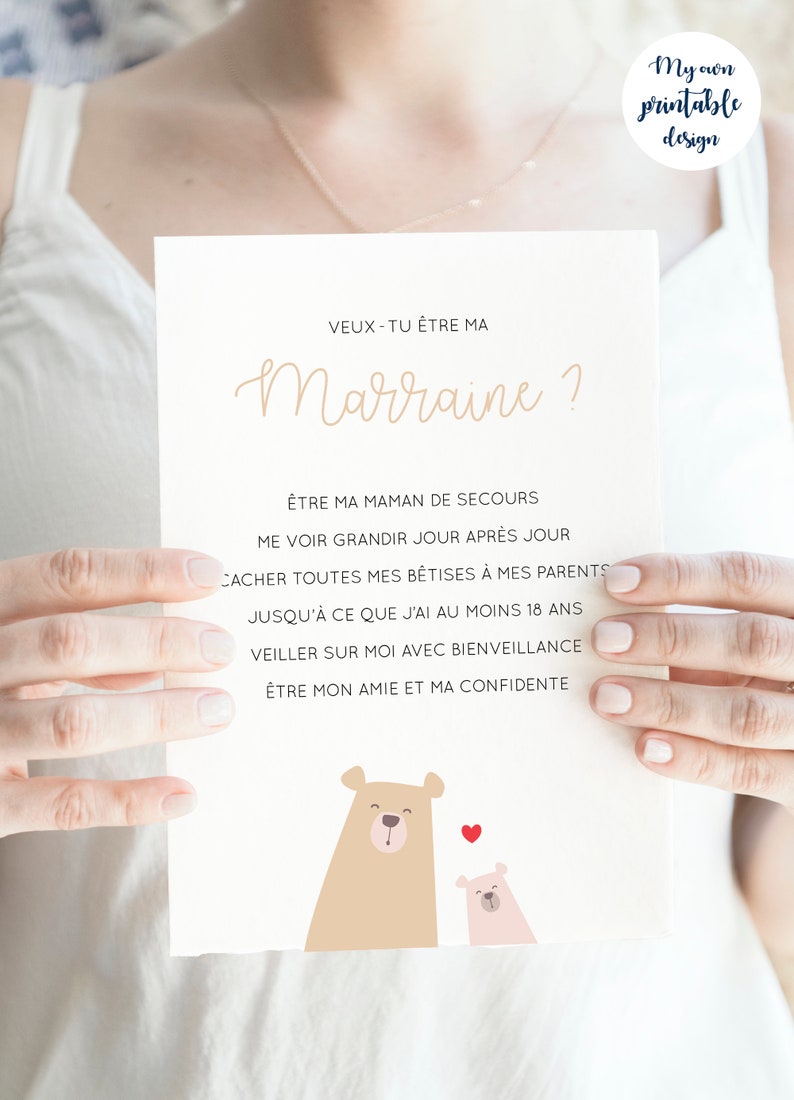 May include: A white card with a brown bear and a pink bear illustration. The card has the text 'VEUX-TU ÊTRE MA Marraine?' and 'ÊTRE MA MAMAN DE SECOURS ME VOIR GRANDIR JOUR APRÈS JOUR CACHER TOUTES MES BÊTISES À MES PARENTS JUSQU'À CE QUE J'AI AU MOINS 18 ANS VEILLER SUR MOI AVEC BIENVEILLANCE ÊTRE MON AMIE ET MA CONFIDENTE'.