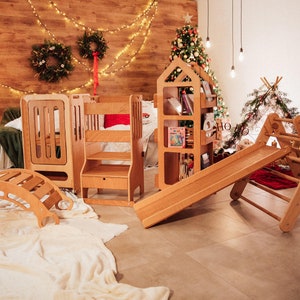 May include: A set of wooden children's toys, including a slide, a climbing frame, a rocking horse, and a bookshelf. The toys are arranged in a room with a wooden floor and a white rug. There are Christmas decorations in the background.