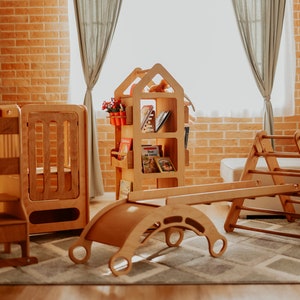 May include: A set of wooden children's play equipment, including a climbing frame, a seesaw, a step stool, and a bookshelf. The equipment is made of natural wood and has a light brown finish.