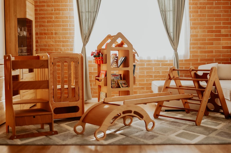 May include: A set of wooden children's play equipment, including a climbing frame, a seesaw, a step stool, and a bookshelf. The equipment is made of natural wood and has a light brown finish.