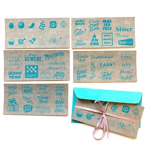 Könnte beinhalten: Ein Satz von 10 braunen Papierkarten mit blauem Text. Die Karten zeigen verschiedene Designs und Sätze, darunter "Bag to the Future", "Let's Talk About Bags", "#Quarter Bag", "Garn Nicht Uebel", "Straffes Gewerbe", "Musterteil", "Schmuck Stuck", "Einzelstückchen", "Garn Nicht Uebel", "Total Genial", "Tetzt!", "Putzig", "Chaaa!", "Unikat", "Cuteness Overload", "Mas Ter Piece", "Sew Much Love", "New Sister", "Brilliant", "Bag Flip", "Hand Made", "Cutie!", "Out Standing", "On Fire", "Bay to Basic", "Bag Street Boys", "Feed the Bag", "Bags and the City", "Bag for Good", "Bags on the Beach", "Jeans Team", "Maro!", "Step by Stepp", "New Jersey", "Goldig", "Gude Laune", "Tip Top!" und "8", "Peace Sign", "Hand", "Chili Pepper", "Bug", "Snake", "Target", "Rocket", "Puzzle", "Bicycle", "Heart".