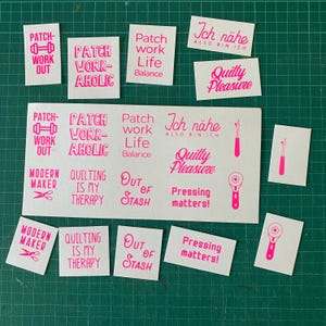 Könnte beinhalten: Eine Sammlung weißer rechteckiger Aufkleber mit pinkfarbenem Text und Symbolen rund ums Nähen und Quilten. Die Aufkleber enthalten Sprüche wie Patch-Work Out, Patchworkaholic, Patch Work Life Balance, Quilty Pleasure, Modern Maker, Quilting Is My Therapy, Out Of Stash, Pressing Matters und Ich nähe also bin ich.