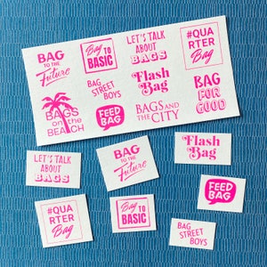 Könnte beinhalten: Eine Sammlung von 12 pinkfarbenen und weißen Aufklebern mit verschiedenen Sprüchen und Designs rund um Taschen. Die Sprüche beinhalten "Tasche in die Zukunft", "Tasche zum Basic", "Lass uns über Taschen reden", "Blitz-Tasche", "Taschen am Strand", "Tasche füttern", "Taschen und die Stadt", "Tasche für immer", "#Viertel-Tasche", "Taschen der Straßenjungs".