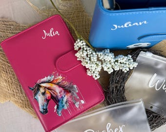 Könnte beinhalten: Ein pinkfarbenes Lederjournal mit dem Namen "Julia" und einem Aquarell-Pferdedesign. Ein blauer Lederordner mit dem Namen "Julian" ist ebenfalls zu sehen. Klare Beutel mit weißer Schrift sind ebenfalls im Bild.