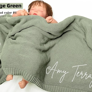 May include: Sage green knitted baby blanket with the name "Amy Terray" in white script. The blanket is wrapped around a baby. The text "Sage Green", "Thread color #1", and "Font: F1" are in the upper left corner.