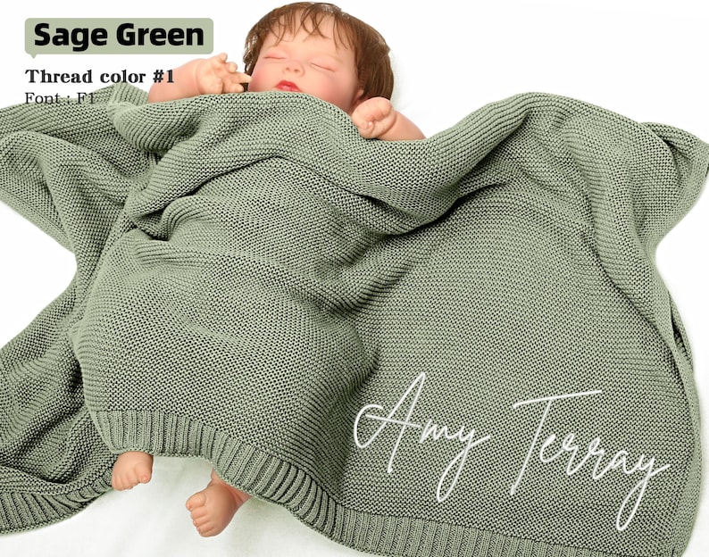 May include: Sage green knitted baby blanket with the name "Amy Terray" in white script. The blanket is wrapped around a baby. The text "Sage Green", "Thread color #1", and "Font: F1" are in the upper left corner.