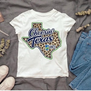 May include: A white short-sleeved t-shirt featuring a graphic of the state of Texas filled with a brown and black leopard print pattern. The text "Choosin' Texas" is printed in dark blue script, with the "UHCL" logo visible in the lower right.