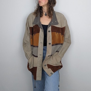 Könnte beinhalten: Eine Wildlederjacke in Beige-, Braun- und Orangetönen mit Knopfleiste. Die Jacke hat ein Patchwork-Design mit verschiedenen Braun- und Orangetönen. Der Kragen ist dunkelgrau. Die Jacke hat zwei Vordertaschen und wird über einem schwarzen Oberteil und einer blauen Jeans getragen.