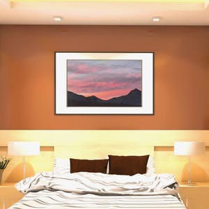 May include: Bedroom interior with a framed landscape painting above a bed. The painting depicts a mountain range under a pink and purple sunset. The bed has brown pillows and a striped comforter. Lamps flank the bed on nightstands.