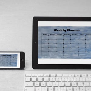 Peut inclure: Une tablette et un smartphone noirs affichant un modèle de planificateur hebdomadaire avec un fond de ciel bleu. Un clavier blanc est au premier plan. La tablette est plus grande que le téléphone, et les deux sont sur une surface claire.