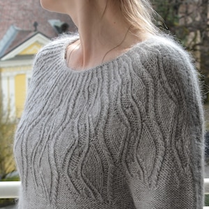 May include: A gray knitted sweater with a cable knit pattern. The sweater has a round neckline and long sleeves.