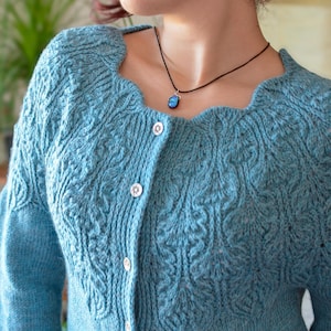 Op de afbeelding: Een lichtblauwe gebreide cardigan met een knoopsluiting en een delicaat kabelbreipatroon. De cardigan heeft een ronde hals en lange mouwen.